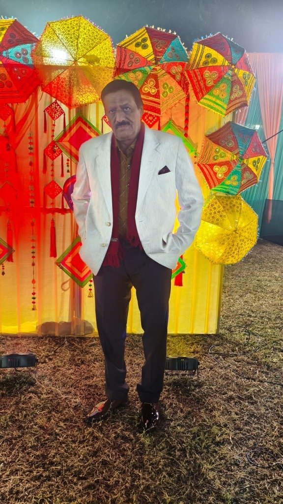 Rajesh Bajaj in white blazer standing before decorative event umbrellas backdrop